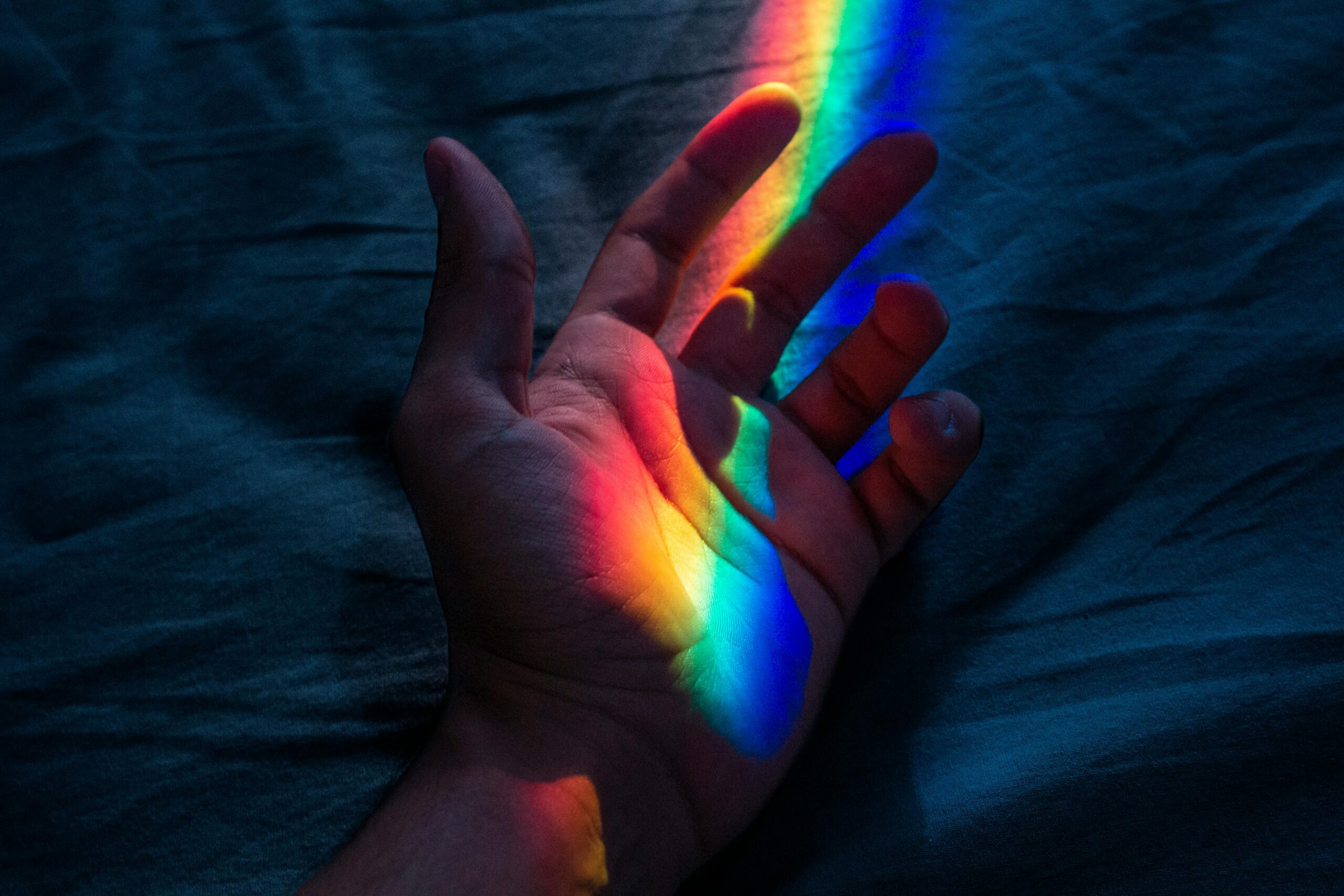 A hand illuminated by a spectrum of rainbow colors in dark ambiance.